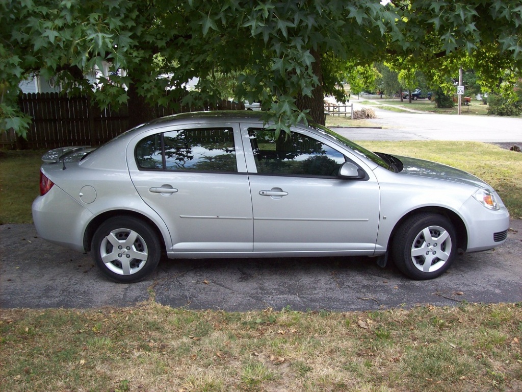 Small silver four-door car sitting on a driveway. The grass is very dry, yellowed, and crunchy since it was mid-July at the time of the photo. 